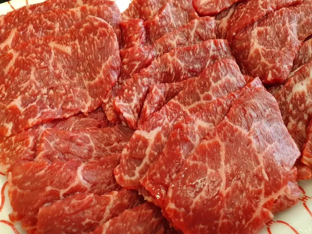 Slices of red marbled meat arranged closely on a white plate