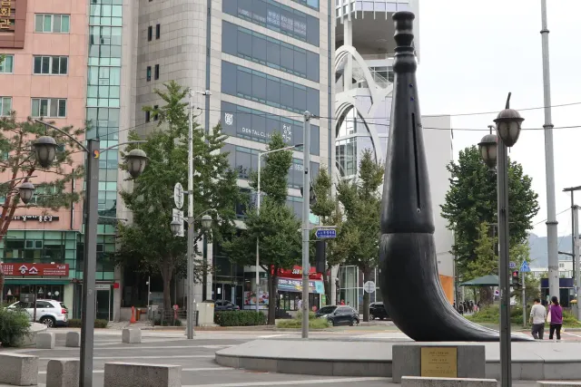 A tall black brush sculpture on a traffic island in a city street