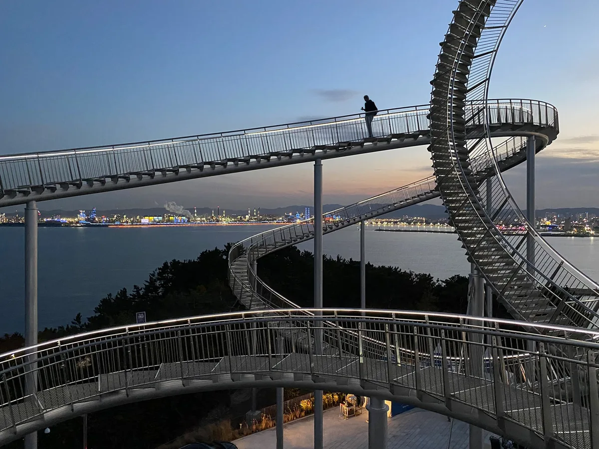 The looping steel Space Walk sculpture in Pohang at dusk with a person walking along the track