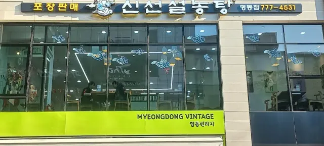 A shopfront with a blue sign, glass windows decorated with clouds and a green band at the bottom