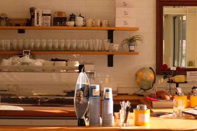 A counter with wooden shelves, glass tumblers, stacks of paper cups and a globe at the side