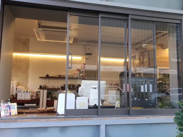 A small stand seen through a wide sliding window, with a counter, a coffee machine and menus