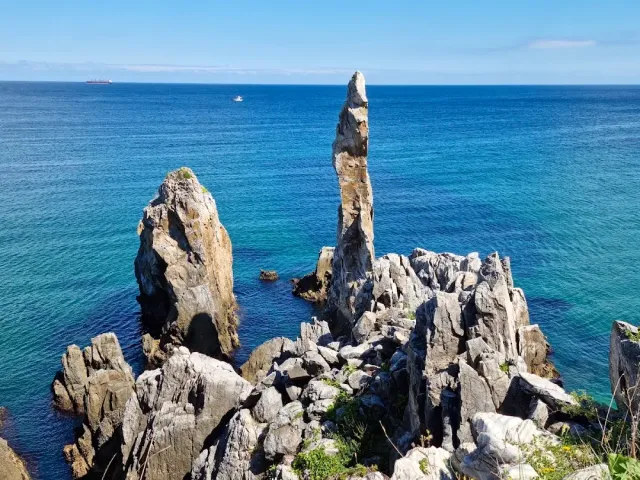A narrow tall rock pillar among white rock teeth facing a blue sea