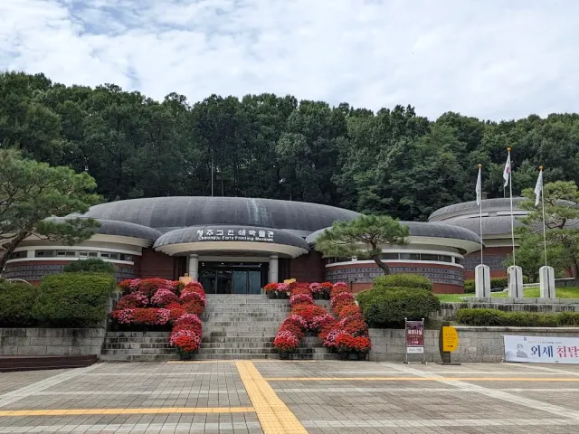 A public building with a dark curved roof, wide steps and beds of red flowers