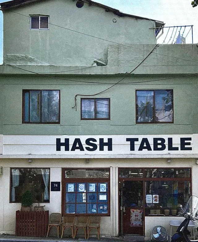 A two storey mint coloured building with a large sign, chairs and a scooter on the pavement