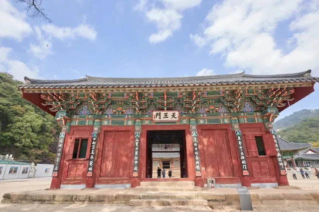 A red wooden gate with beams painted green and gold, facing green mountains