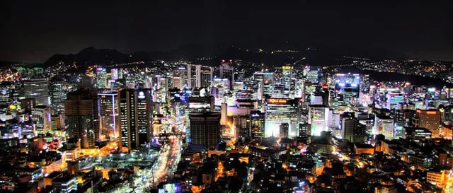 A sea of city lights and skyscrapers spread out from above at night