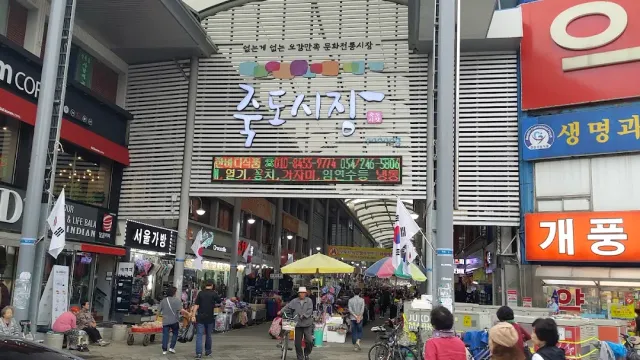 An arched market entrance with a colorful sign, shoppers and stalls behind it