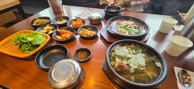 Two steaming pots of soup with meat and green onion, surrounded by small side dishes