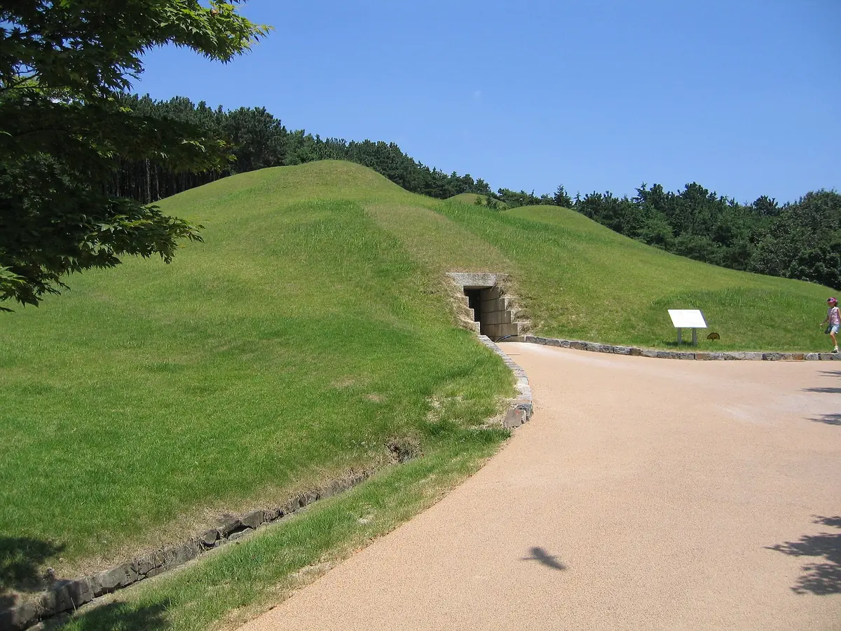 Grass covered burial mounds with a dark stone entrance, and a paved path alongside