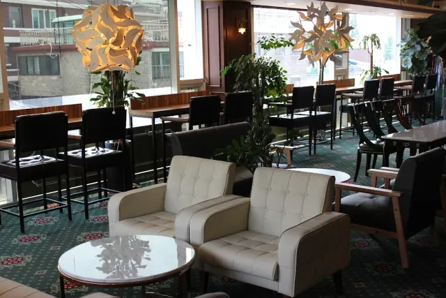 A retro space with a patterned green carpet, white leather armchairs and large hanging lamps