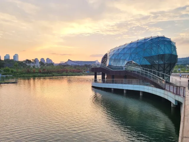 A rounded blue glass building on a lakeshore at pink sunset