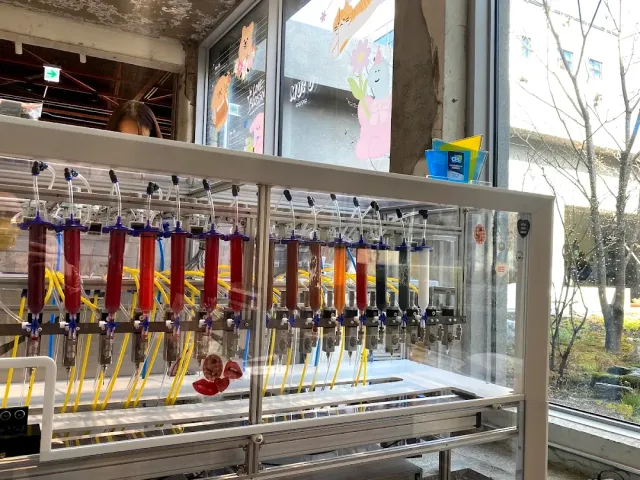 A machine behind glass with a row of syringes in different colors and yellow tubes