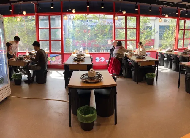 A hall with red window frames, tables holding round grills and seated diners