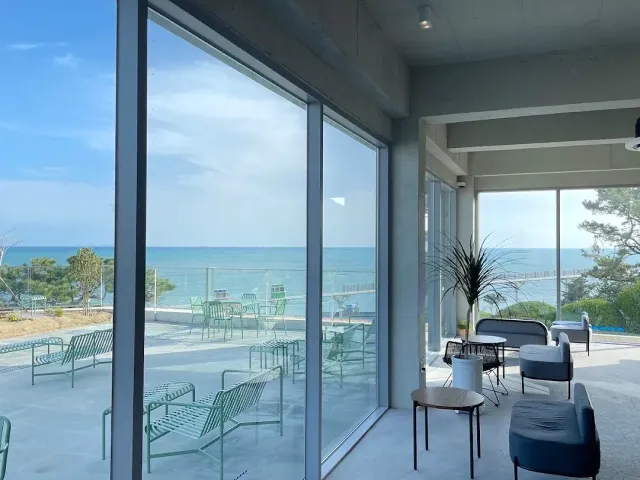 A bright space with glass walls facing the sea, metal chairs on the terrace and grey armchairs