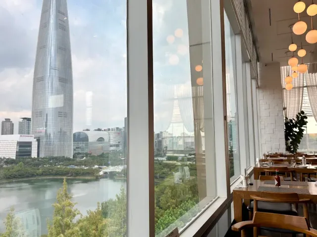 A window with a view of a tall tower and a lake, wooden tables and hanging globe lamps