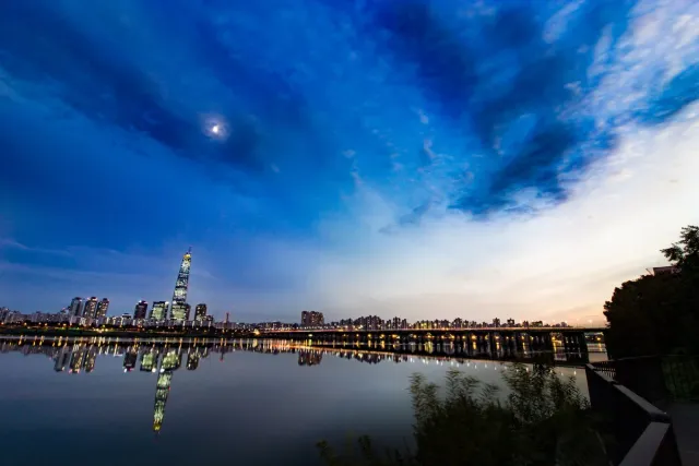 A slender tapering tower rising above a reflecting river at dusk
