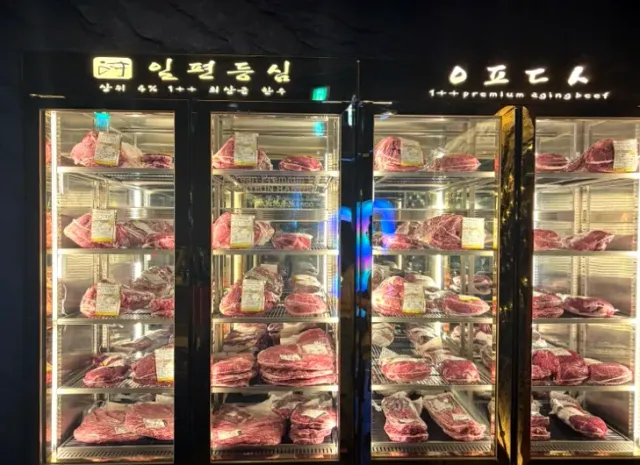 Lit glass fridges holding red cuts of meat arranged on shelves