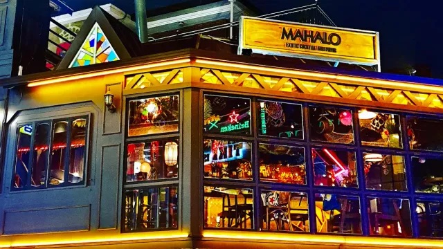 A bar facade lit in gold at night with wide windows and neon signs inside