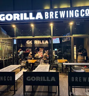 A lit brewery front in the evening with wooden benches outside and diners inside