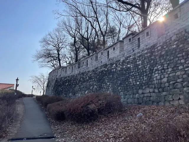 An ancient stone wall with battlements along a path, bare trees and a low sun