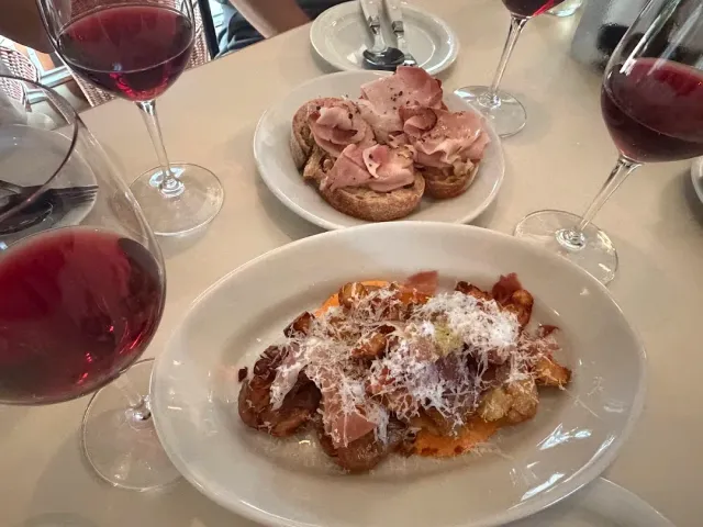 A table with glasses of red wine, bread slices with cold cuts and a plate with grated cheese