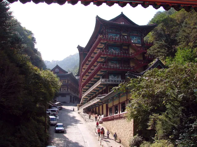 A multi storey tiled temple building wedged between forested slopes