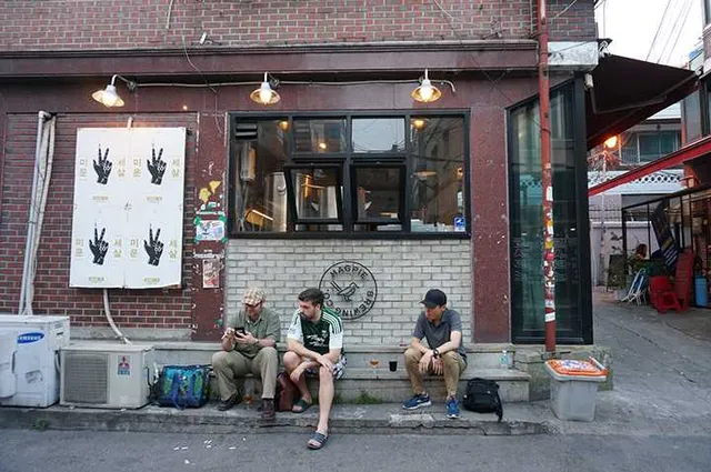 Three people sitting on a step in front of a brick facade with a large window and lamps