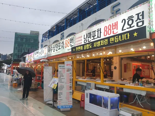Food stalls with huge banners and lights, a person with an umbrella on a wet promenade