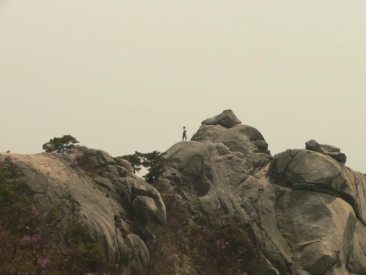 Bare granite domes at a mountain summit, with a lone hiker standing on one of them