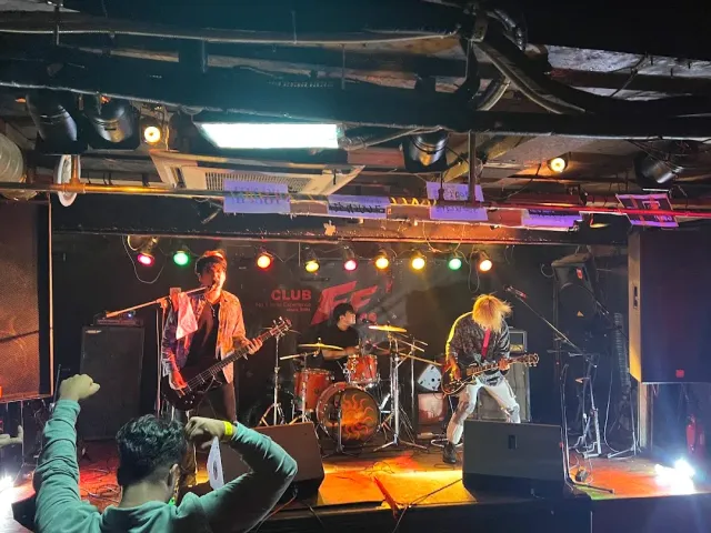 A band playing on a small stage under coloured lights, with the crowd raising hands in front