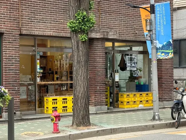 A brick front with display windows, yellow plastic crates outside and a tree on the pavement