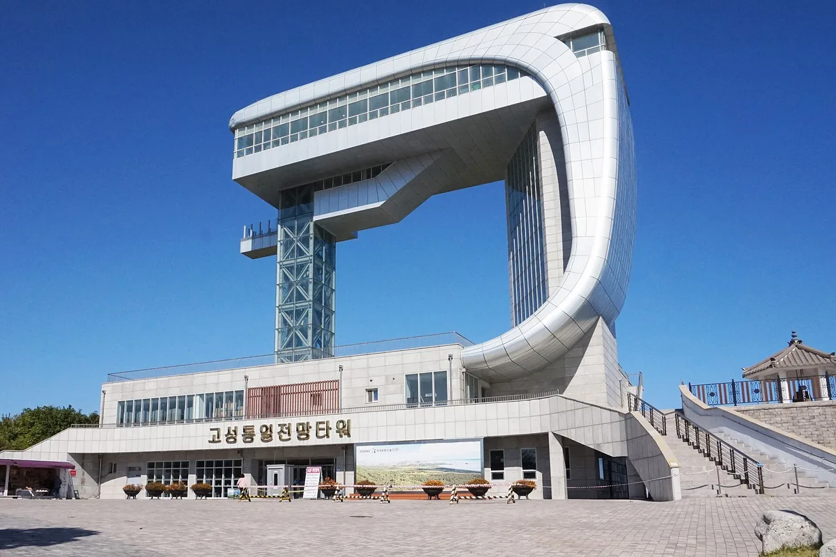 Modern observation building shaped as a great arc above a stone base against a bright blue sky