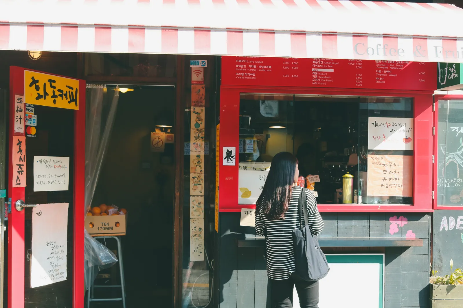 The front of a small red painted coffee shop with a customer at the counter in Seoul, South Korea