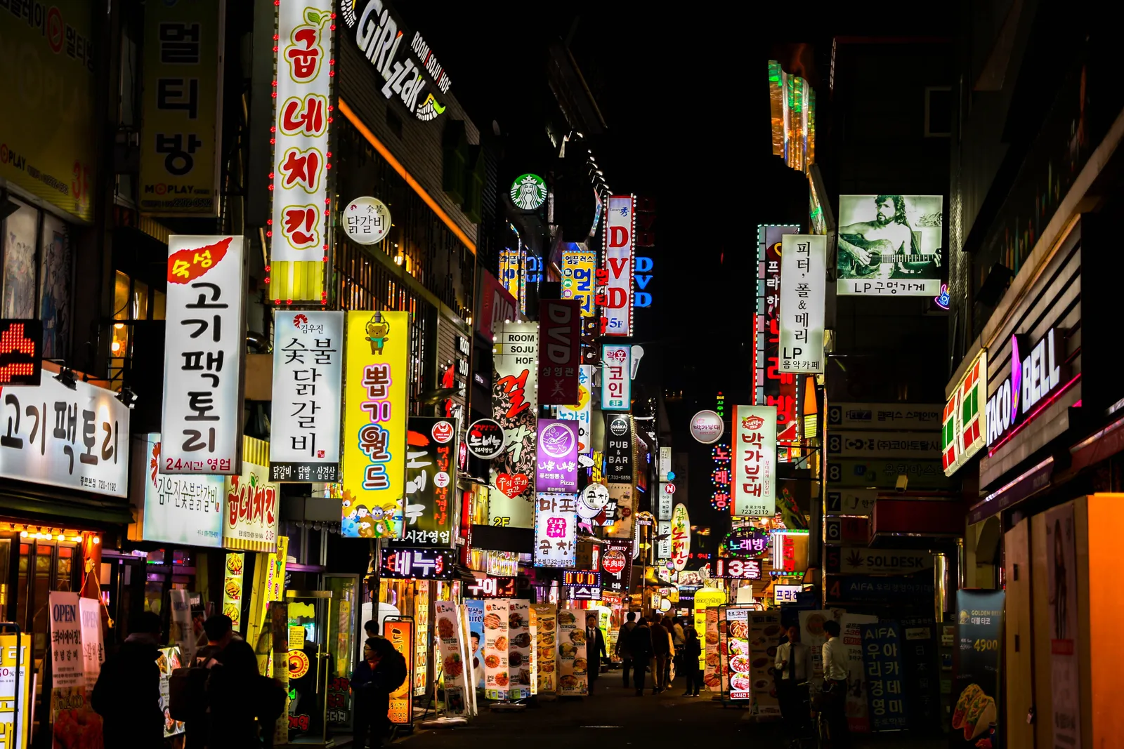 A street in Seoul at night packed with Korean neon signs for bars and restaurants