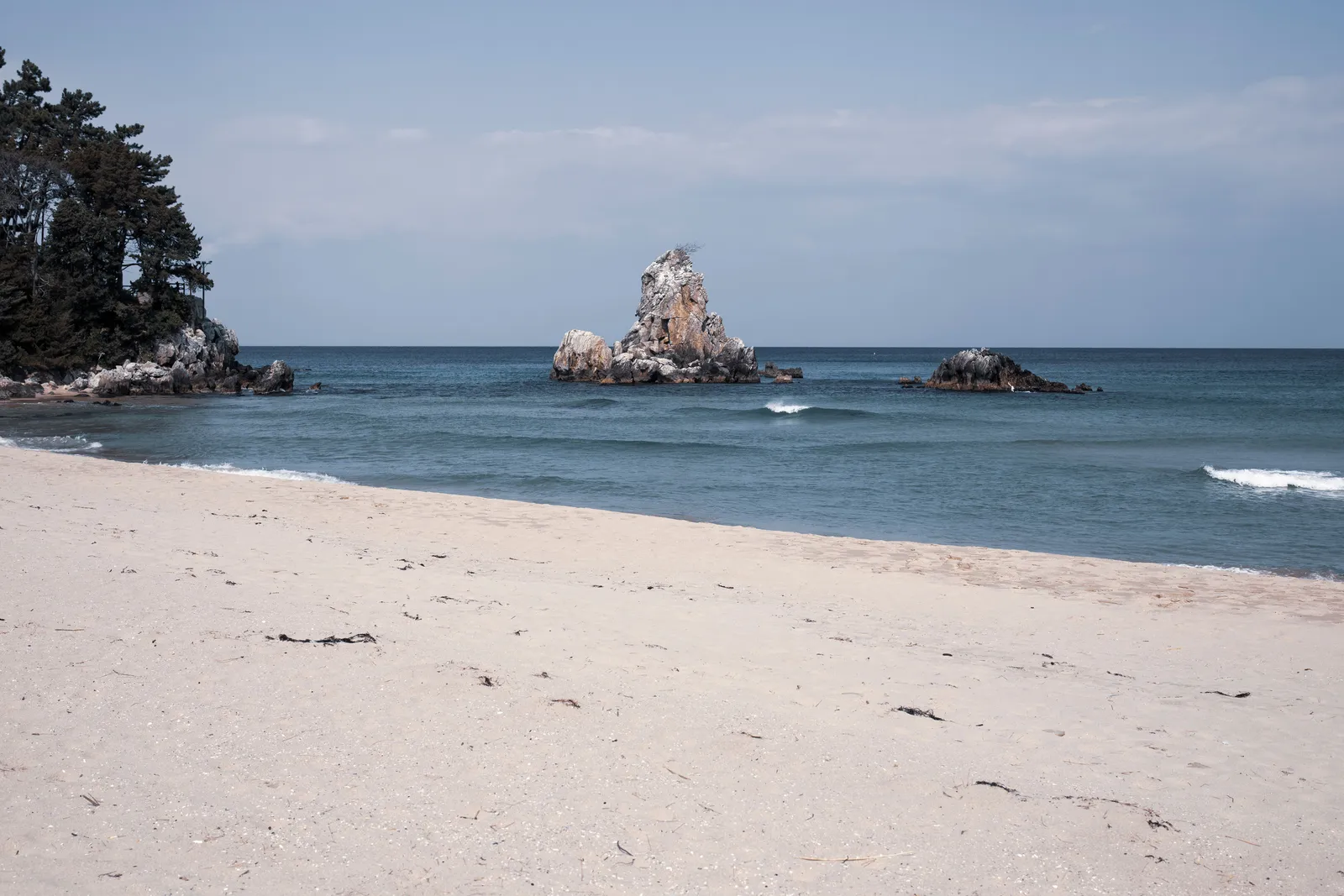 A quiet sand beach on Geoje Island with clear water and low hills in the background, South Korea