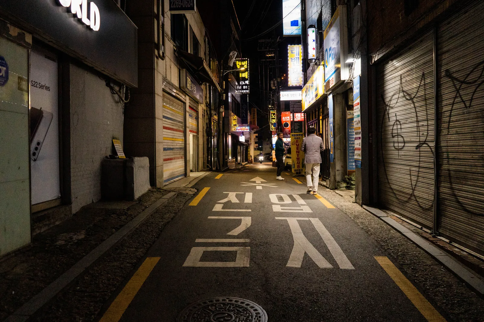 A narrow street of bars and shops lit up at night in the Hongdae district of Seoul, South Korea